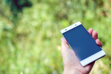 Female hand holding a smartphone on a background of green grass