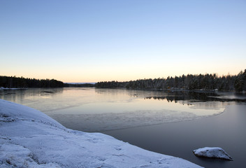 A cold morning in Finland. Amazing scenery just after sunrise. First snow is on the ground and the lake is about to freeze.