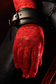 Eine Hand in rotem Spitzenhandschuh und Lederfessel am Handgelenk