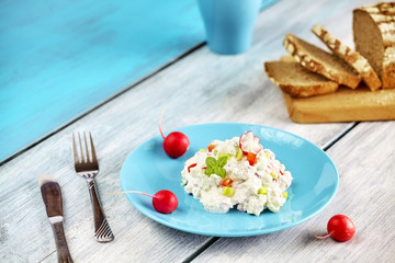 Cottage cheese with radish on a blue plate, healthy breakfast on rustic wooden table.