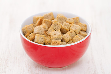 croutons in red bowl on white wooden background