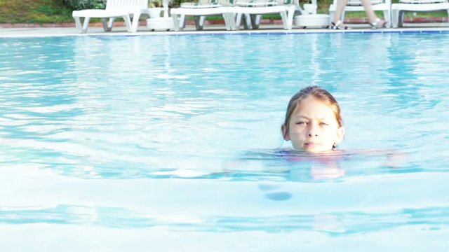 happy little girl swims in the pool with blue water