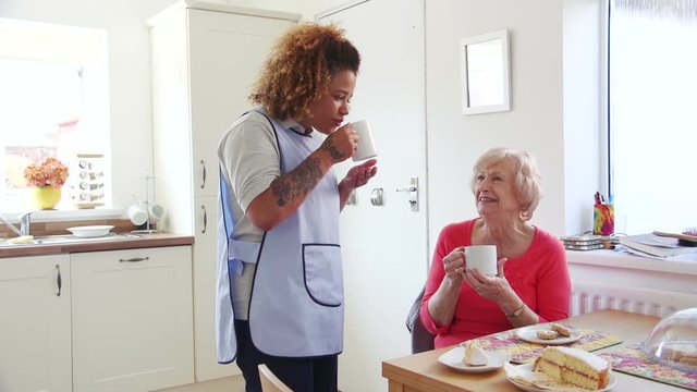 Senior woman talking to her home caregiver over a cup of tea and some cake.