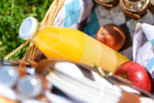 Picnic Basket With Orange Juice Bottle, Apples, Peaches, Oranges And Croissants On Green Grass In Spring