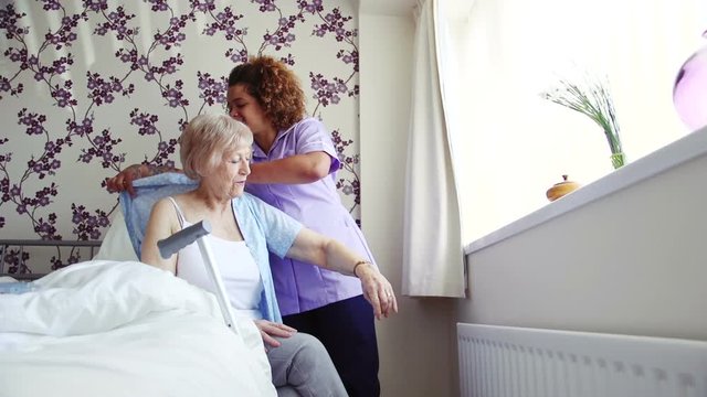 Home caregiver helping a senior woman get dressed in the bedroom of her home.