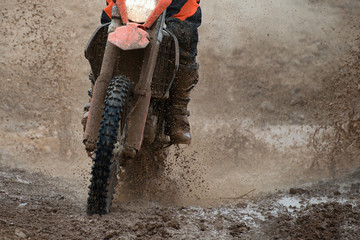 Motocross driver splashing mud on wet and muddy terrain