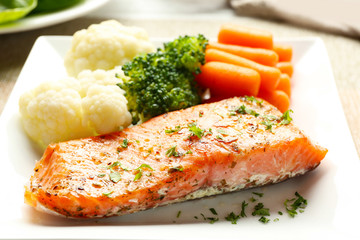 Piece of salmon with vegetables on plate closeup