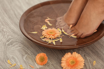 Female feet in spa bowl on wooden background