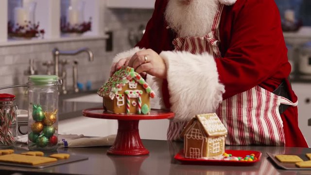 Santa Claus in kitchen decorating gingerbread house