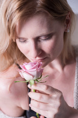 beautiful blonde woman is smelling at a rose in her hand