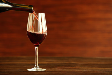 Red wine pouring into a glass on wooden background
