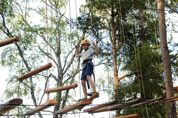 Portrait of active brave boy enjoying outbound climbing at adventure park on tree top