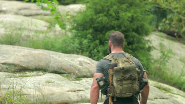 Handheld shot of a male hiker backpacking on large boulders.