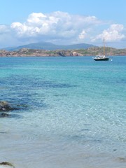 Single yacht and crystal clear blue green water in the Sound of Iona, Scotland, with view towards distant Mull hills