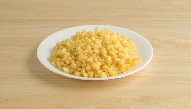Shoepeg white corn with a butter sauce on a dish atop a wood table.