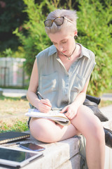 Young handsome caucasian blonde italian designer sitting on a small wall, using smartphone and tablet and sketching on a notebook - creativity, enlightenment, working concept