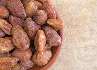 Honey glazed almonds in a small bowl atop an old wood cutting board.