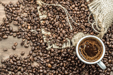 Cup of coffee and coffee beans on wooden table, overhead