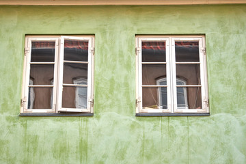 Two white painted danish colonial style windows fastened in a green plastered facade in Elsinore city, with reflections from an opposite old building