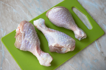 Three chicken legs are on the green cutting board