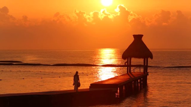 Woman walks along dock during sunset at tropical resort