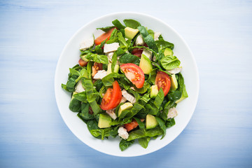 Fresh healthy salad with chicken, tomatoes, spinach and avocado on blue wooden background top view. Health and food.