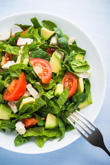 Fresh healthy salad with chicken, tomatoes, spinach and avocado on blue wooden background top view. Health and food.