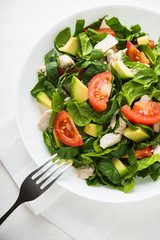 Fresh salad with chicken, tomatoes, spinach and avocado on white wooden background top view. Healthy food.