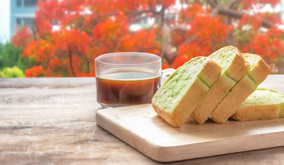 Bread slices placed on a wooden floor with black coffee near a window with a nice view.