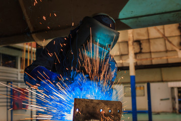 Worker is welding metal in factory.