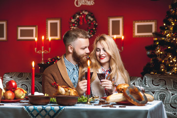 Beautiful couple in a decorated festive interior with a Christmas tree drinking wine. A romantic dinner for thanksgiving with fried chicken and candles