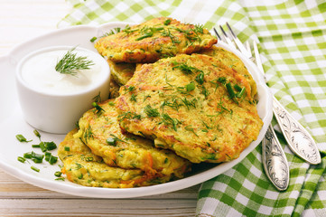 Fritters with zucchini and carrots on white wooden background.