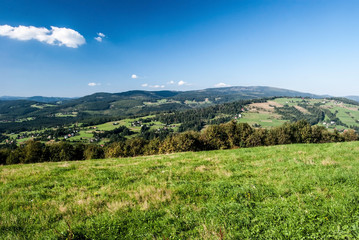 Fototapeta na wymiar nice view from Ochodzita hill in Beskid Slaski mountains with hills, meadows, fields and settlement of Koniakow village during nice summer day with blue sky and clouds