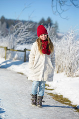 Adorable little  girl walking in winter forest on a sunny day