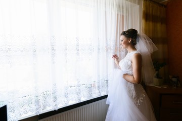 Young bride in white dress looking out the window.