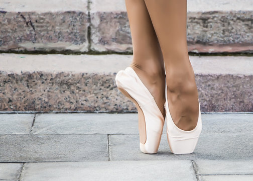 Feet dressed in dance pointe shoes, sports shoes on the background of stone steps. Sexy female legs. 