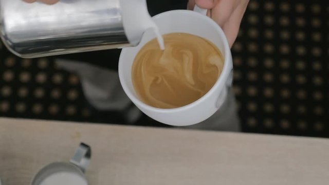 Close-up shot of barista making latte with milk flower picture on the top and serving coffee