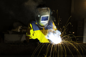 The worker welding metal in manufacturing plant, sparks flying..