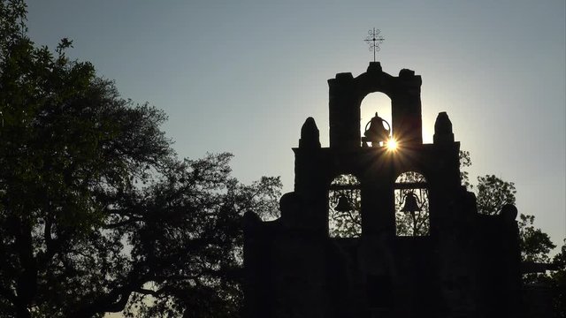 Spanish Mission Espada church bells in silhouette as the sun sets behind mission in San Antonio, Texas