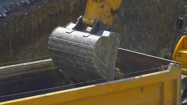 Slow motion - Excavator loading soil on a dump truck. Crawler dozer and tipper working at the construction site. Close up video
