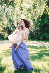 Naklejka premium Lifestyle group portrait of smiling white Caucasian brunette mother holding hugging daughter in pink dress dancing with baby child on sunny summer day in park