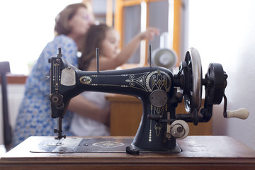 Old sewing machine in a sewing workshop. Dressmaker and her granddaughter making a dress