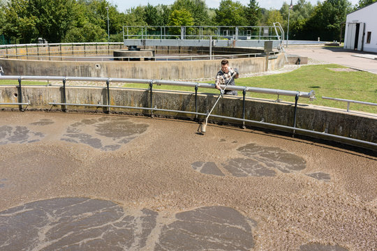 Worker taking water sample out of clarifier tank of sewage treatment plant