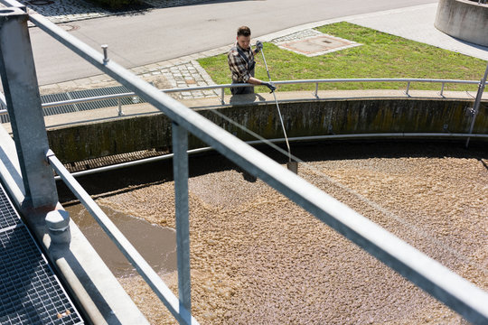 Worker Taking Water Sample Out Of Clarifier Tank Of Sewage Treatment Plant