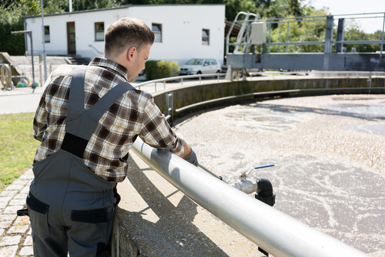 Worker taking water sample out of clarifier tank of sewage treatment plant