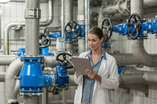 Laboratory technician checking report on tablet computer in pipe room of wastewater treatment plant
