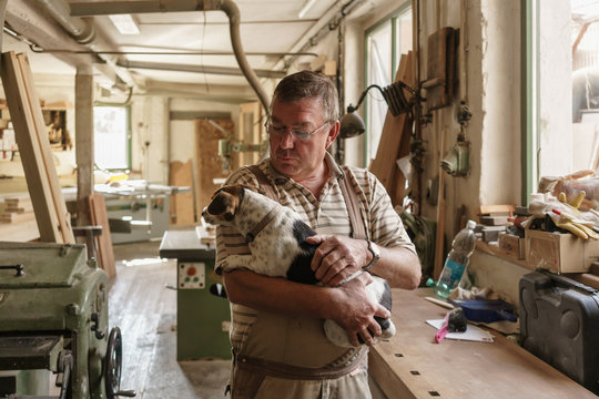 Senior Craftsman beginning day in his wood workshop by petting his dog