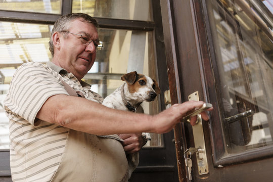 Carpenter carrying little dog and opening front door to his work