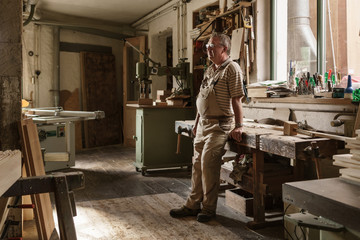 Carpenter in his wood  workshop taking rest by leaning on workbe