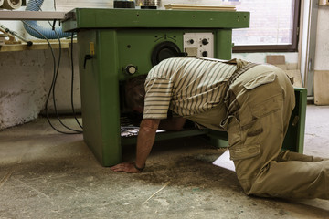 Craftsman in carpentry workshop checking machine down on his knees